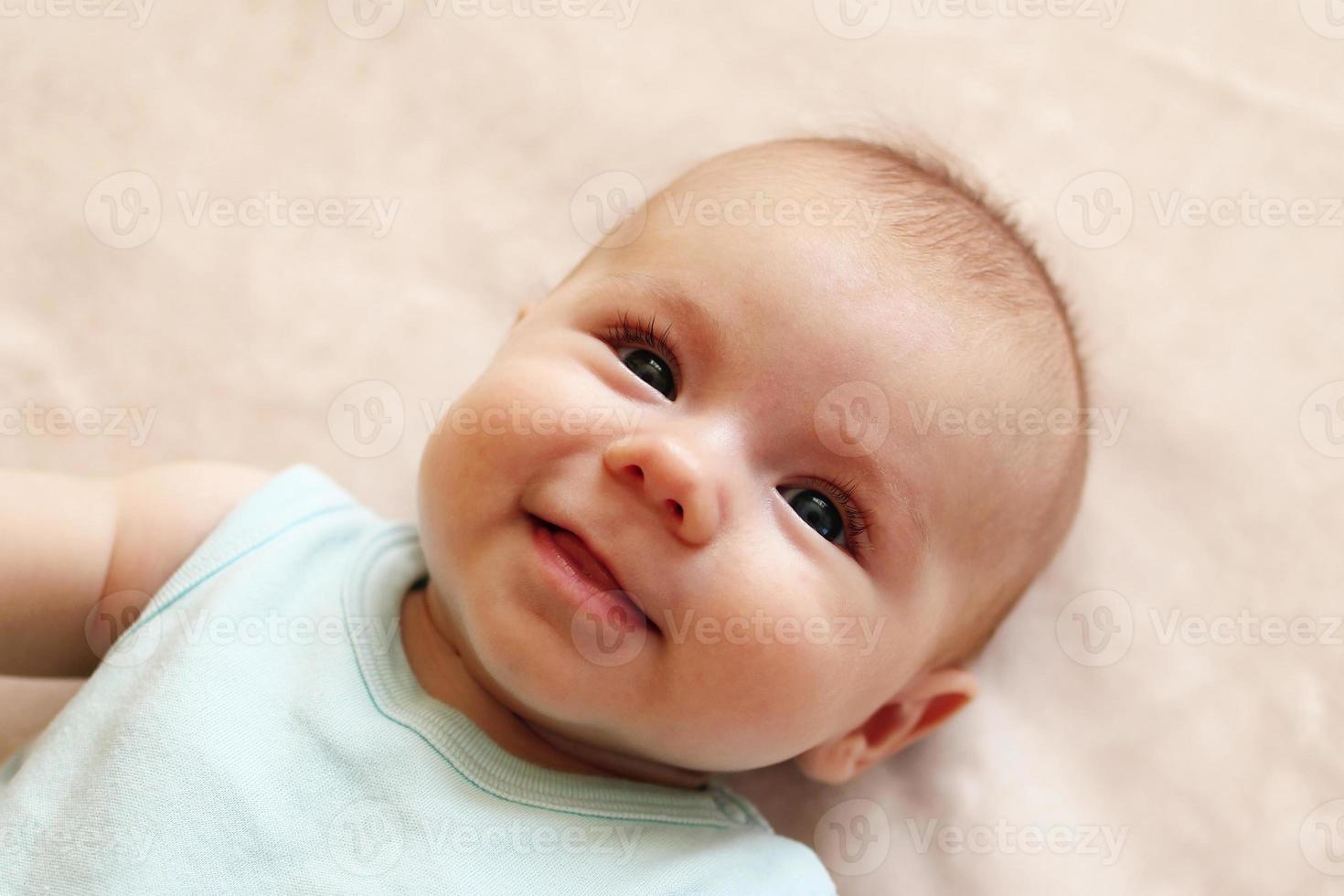 portrait d'un mignon bébé souriant en body bleu sur une couverture beige. photo
