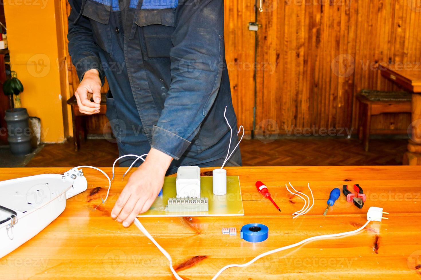 un homme travaillant électricien travaille, recueille le circuit électrique d'un grand réverbère blanc avec des fils, un relais dans une usine industrielle photo