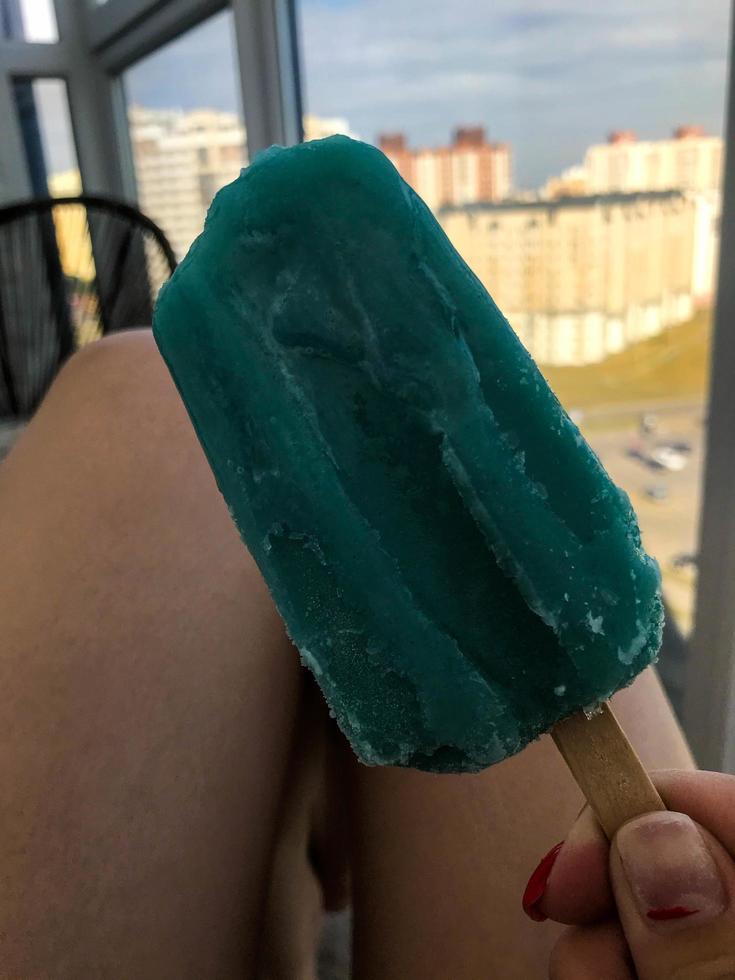 fille avec de la glace turquoise dans les mains est assise sur le balcon sur fond de coucher de soleil. belle vue sur la ville depuis l'étage supérieur. crème glacée avec de la glace et de la neige. glace aux fruits photo