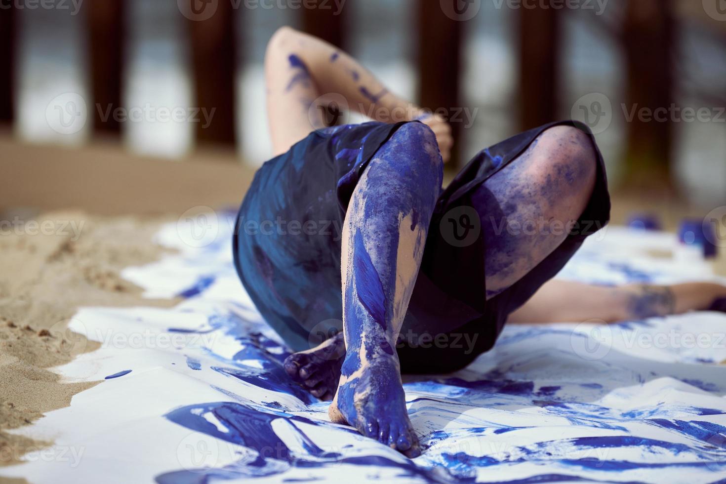 artiste de performance féminine en robe bleu foncé enduite de peinture à la gouache bleue avec de larges traits sur toile photo