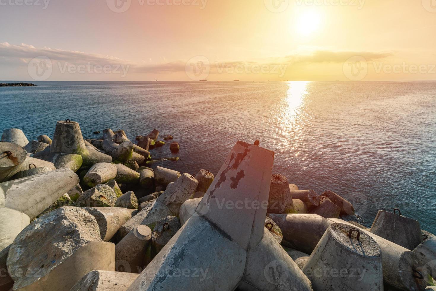 beau paysage marin au coucher du soleil. rêves de voyage et motivation. brise-lames tétrapodes sur le rivage de la jetée. cargos à l'horizon. photo