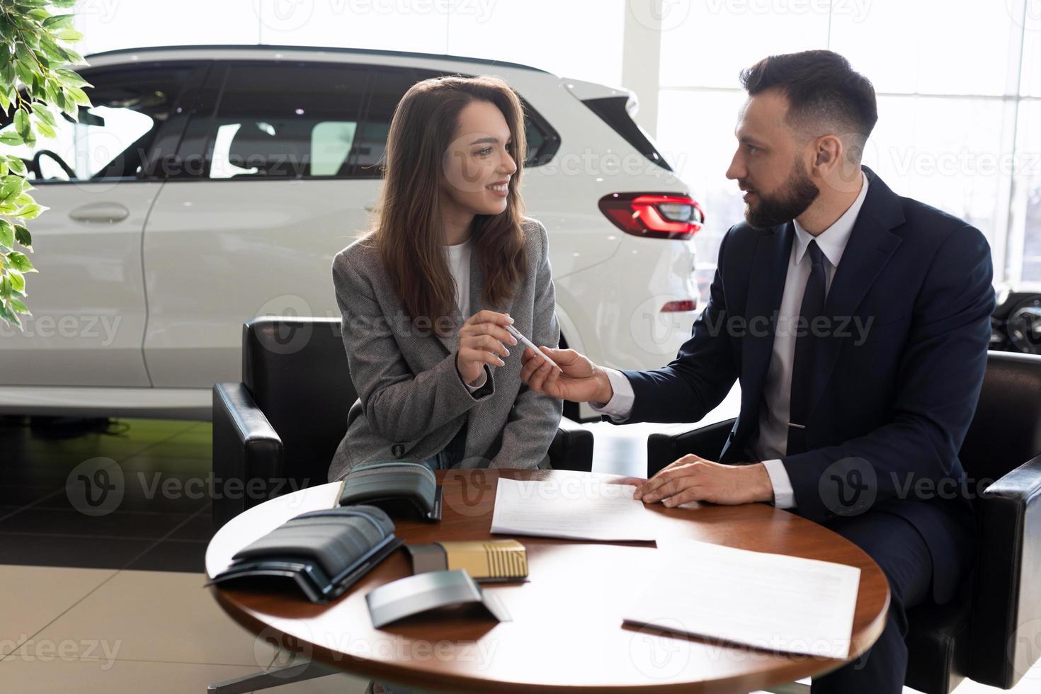 directeur masculin vendant une nouvelle voiture à une jeune femme dans un concessionnaire automobile, concept de location de voiture photo