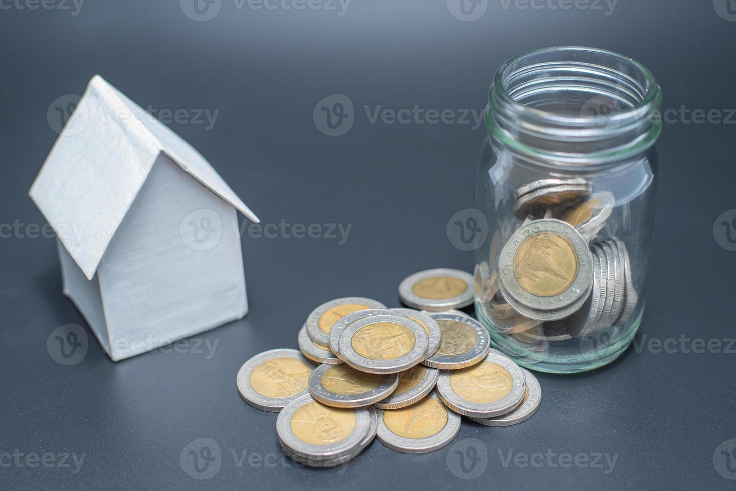 pièces de monnaie de la thaïlande dans un bocal avec des pièces en tas sur fond noir avec modèle de maison photo