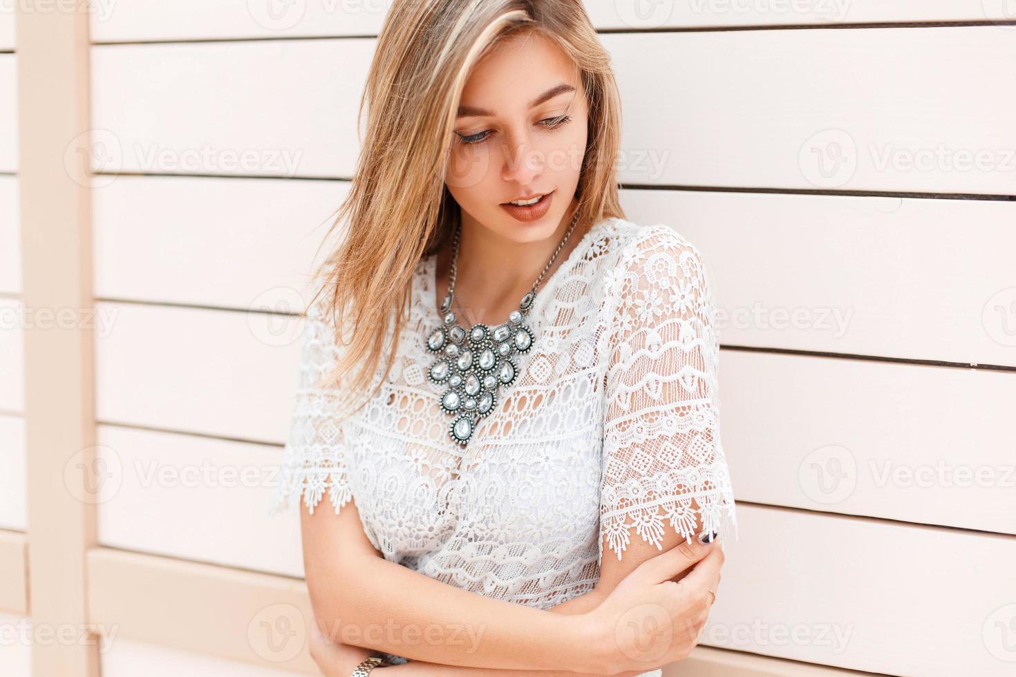 belle jeune fille en blouse de dentelle blanche regardant vers le bas près d'un mur en bois photo