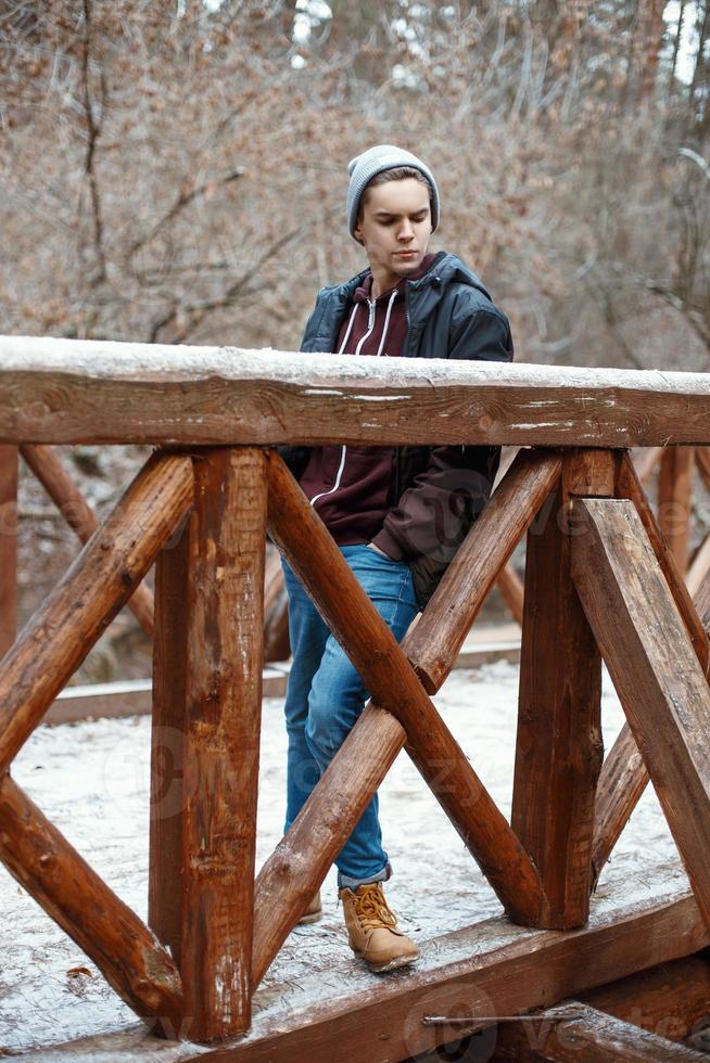 jeune bel homme se tient sur un pont en bois sur le fond de la forêt d'hiver photo