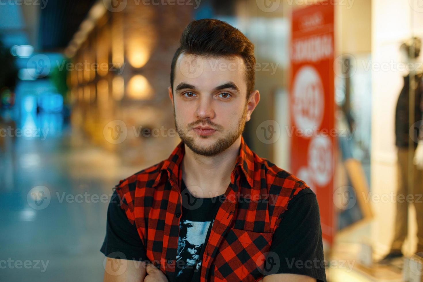 jeune beau mec en chemise rouge sur le fond d'un centre commercial avec une vitrine photo