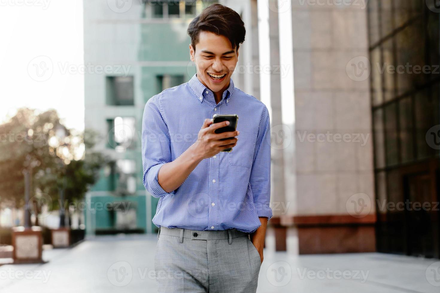 portrait d'un jeune homme d'affaires heureux utilisant un téléphone portable dans la ville urbaine. mode de vie des gens modernes. vue de face. bâtiment moderne en arrière-plan photo