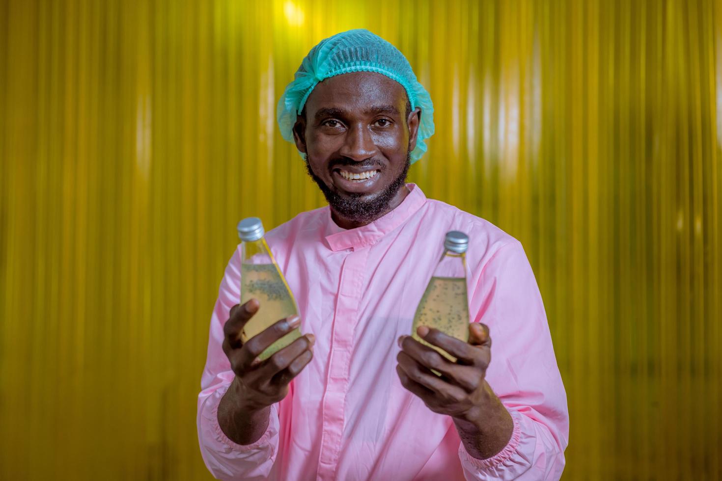 ouvrier scientifique dans une usine de boissons en bouteilles portant un chapeau de sécurité posant un travail de démonstration pour vérifier la qualité des produits de graines de basilic sur le tapis roulant avant la distribution aux entreprises du marché. photo