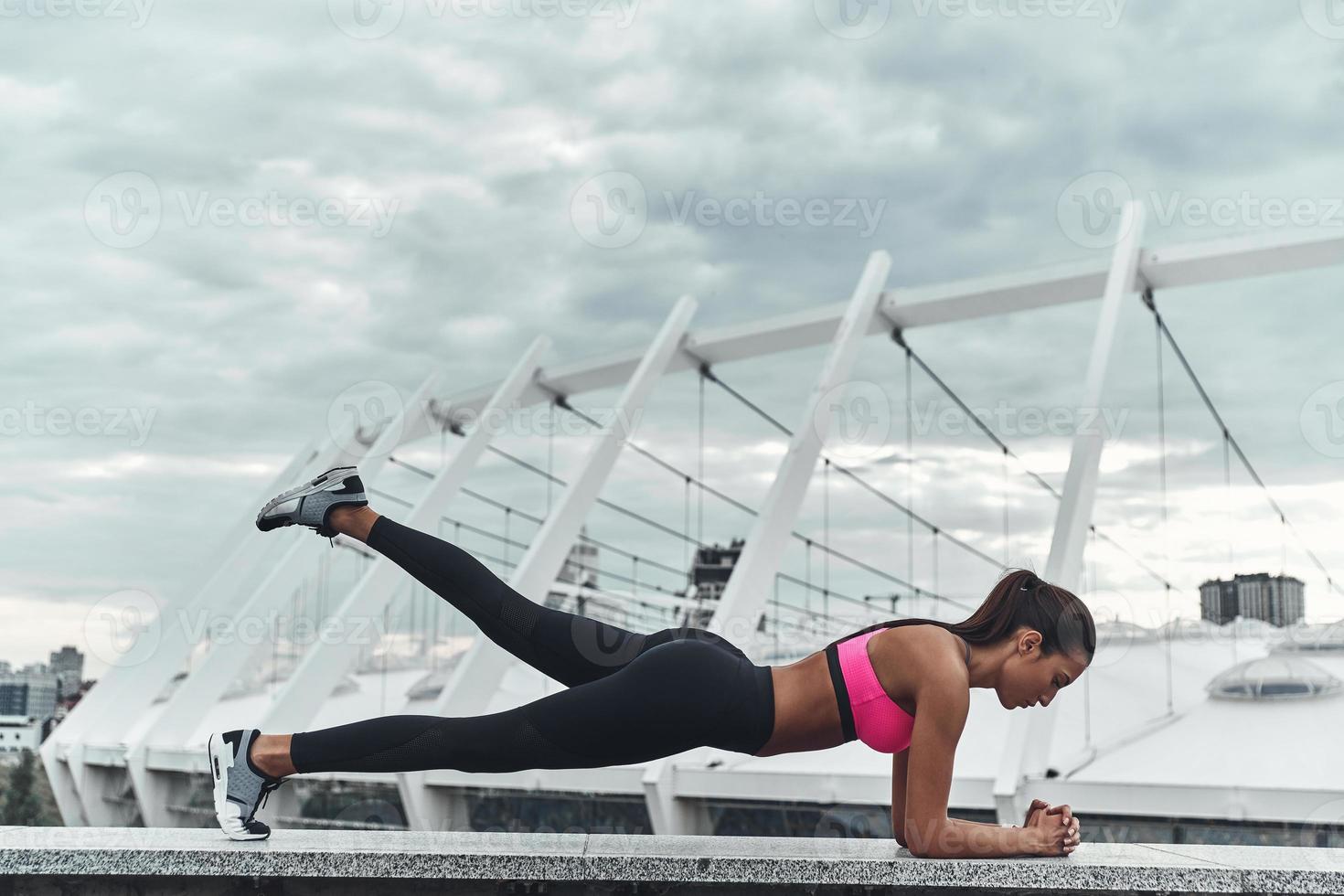 entraînement du matin. jeune femme moderne en vêtements de sport gardant la position de la planche tout en faisant de l'exercice à l'extérieur photo