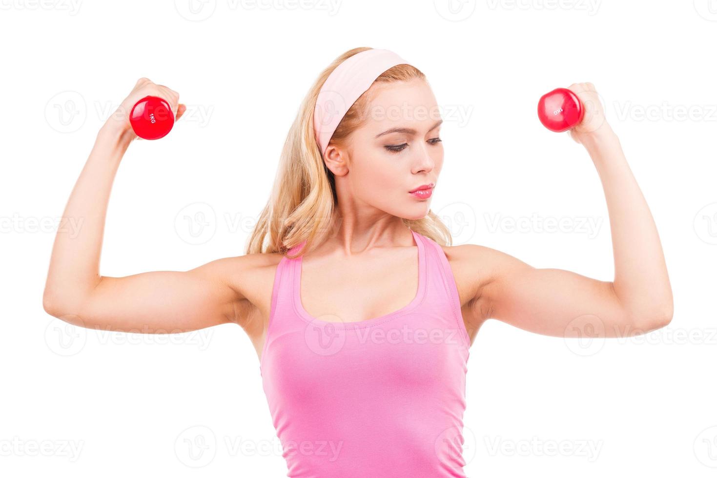 beauté adaptée. Belle femme aux cheveux blonds pin-up en chemise rose faisant de l'exercice avec des haltères en se tenant debout isolé sur fond blanc photo