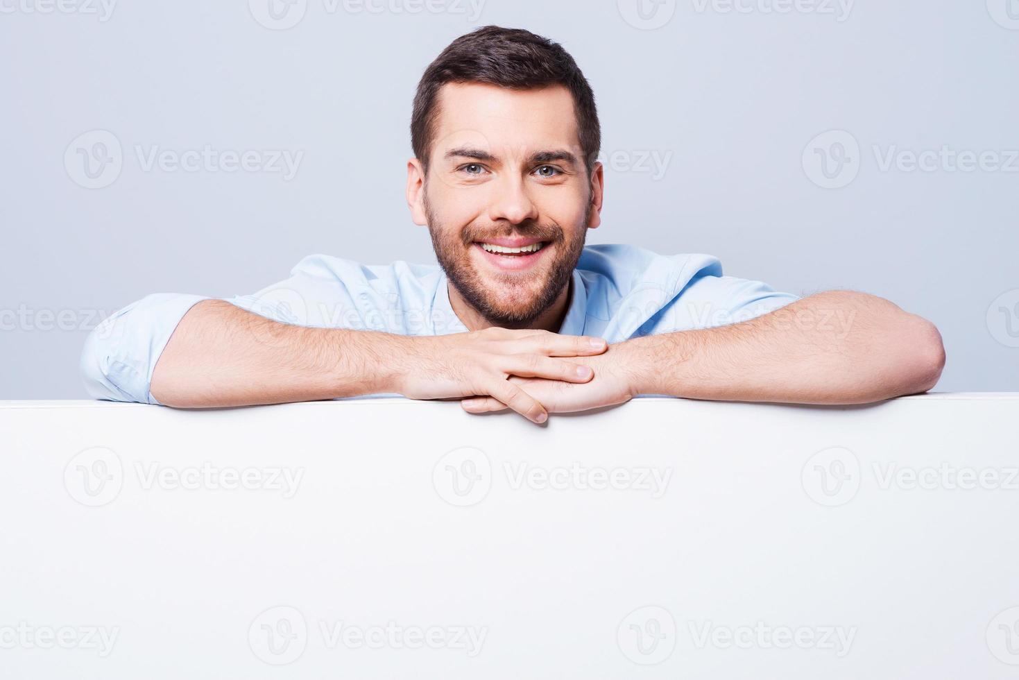 se penchant sur l'espace de copie. beau jeune homme se penchant à l'espace de copie en se tenant debout sur fond gris photo