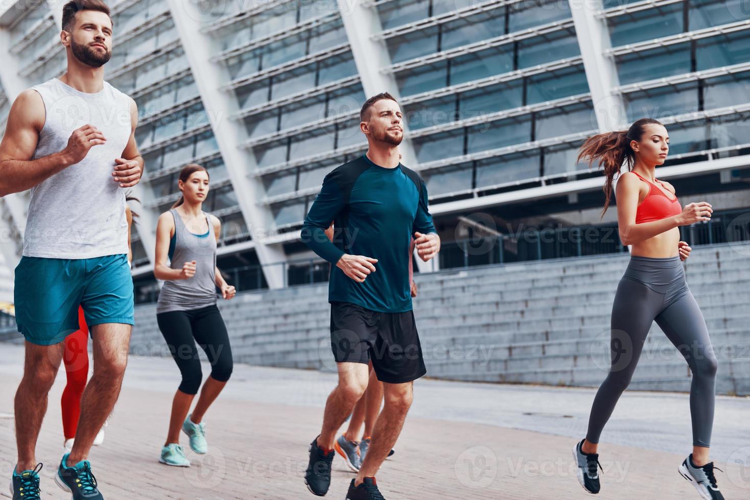 groupe de jeunes en vêtements de sport faisant du jogging tout en faisant de l'exercice sur le trottoir à l'extérieur photo