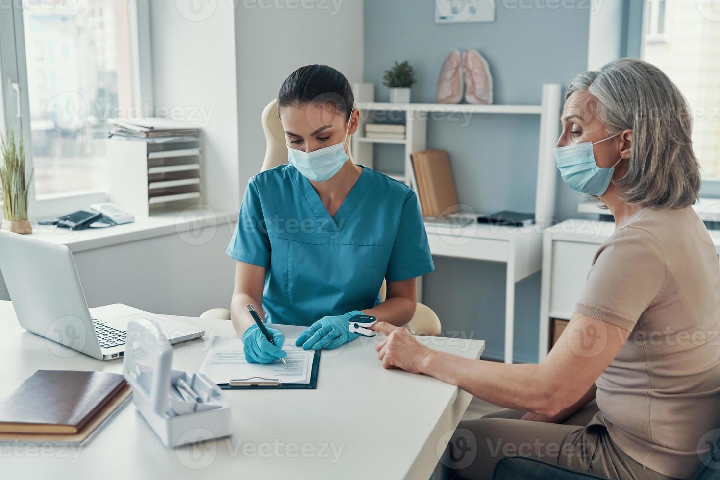 jeune femme paramédicale utilisant un équipement de surveillance pour vérifier le pouls d'une femme mature tout en travaillant à l'hôpital photo