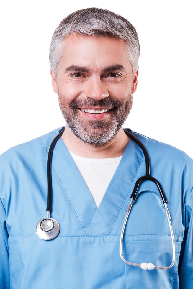 portrait de confiance et d'expérience. portrait d'un chirurgien mature heureux en uniforme bleu regardant la caméra et souriant tout en se tenant isolé sur blanc photo