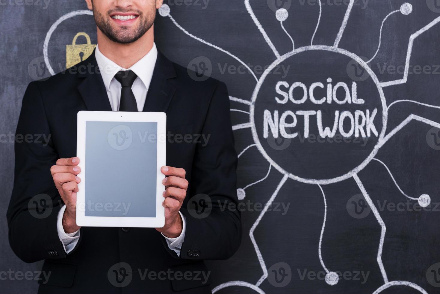 gadget aidant à être moderne. image recadrée de l'homme en tenues de soirée tenant une tablette numérique en se tenant debout contre le dessin à la craie du réseau social sur le tableau noir photo