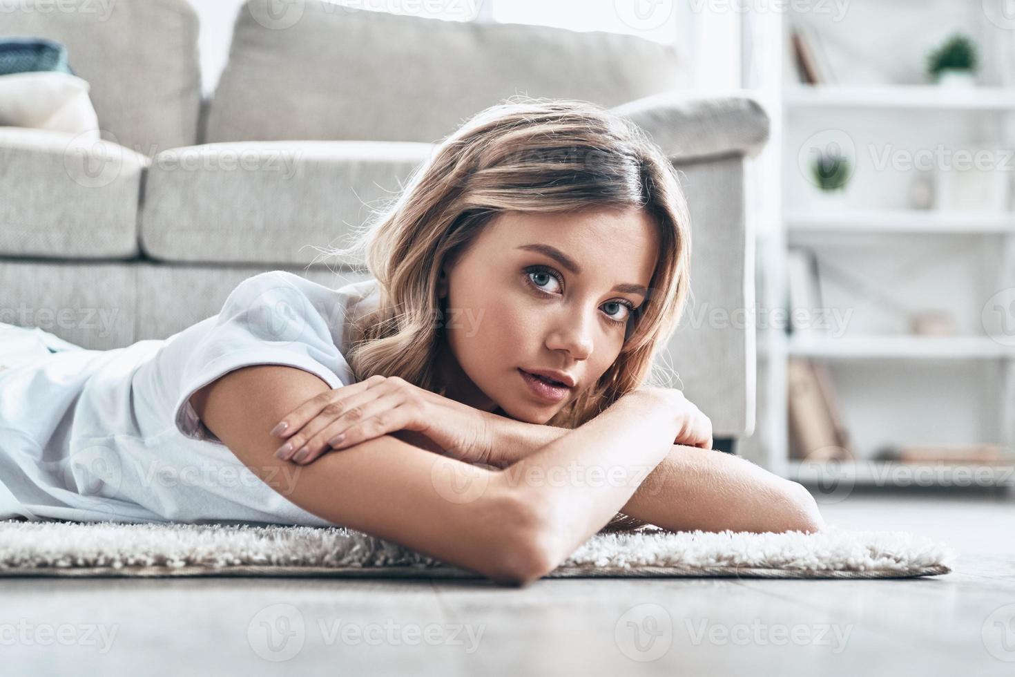 week-end paresseux. belle jeune femme regardant la caméra et souriant en position couchée sur le sol à la maison photo