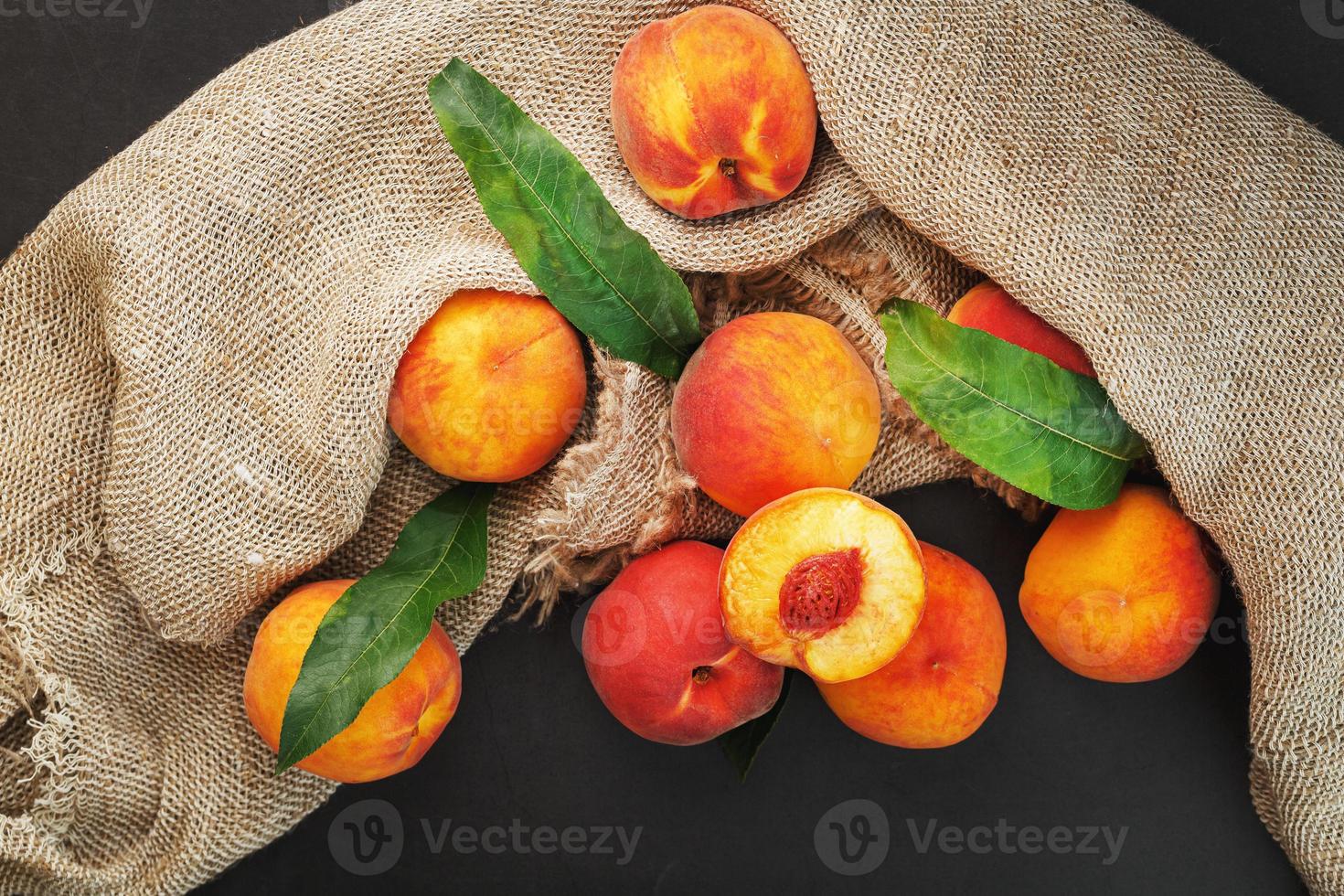 fruit de pêche sur fond noir avec un tissu de toile de jute et de feuilles vertes. photo