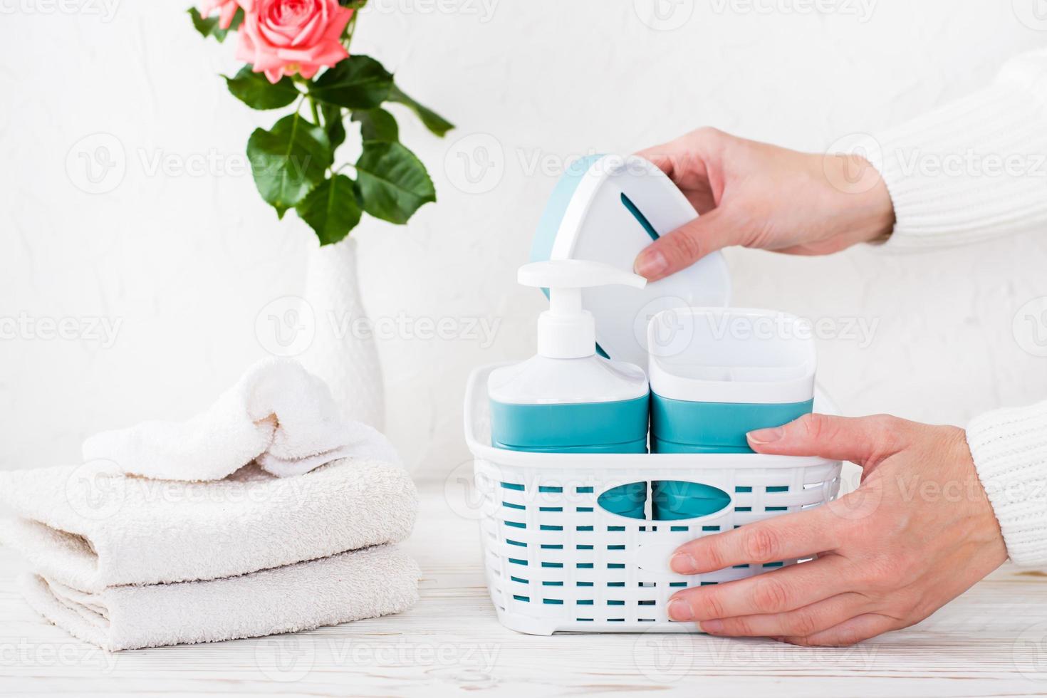 les mains des femmes mettent des accessoires de salle de bain dans un panier et une pile de serviettes sur la table photo