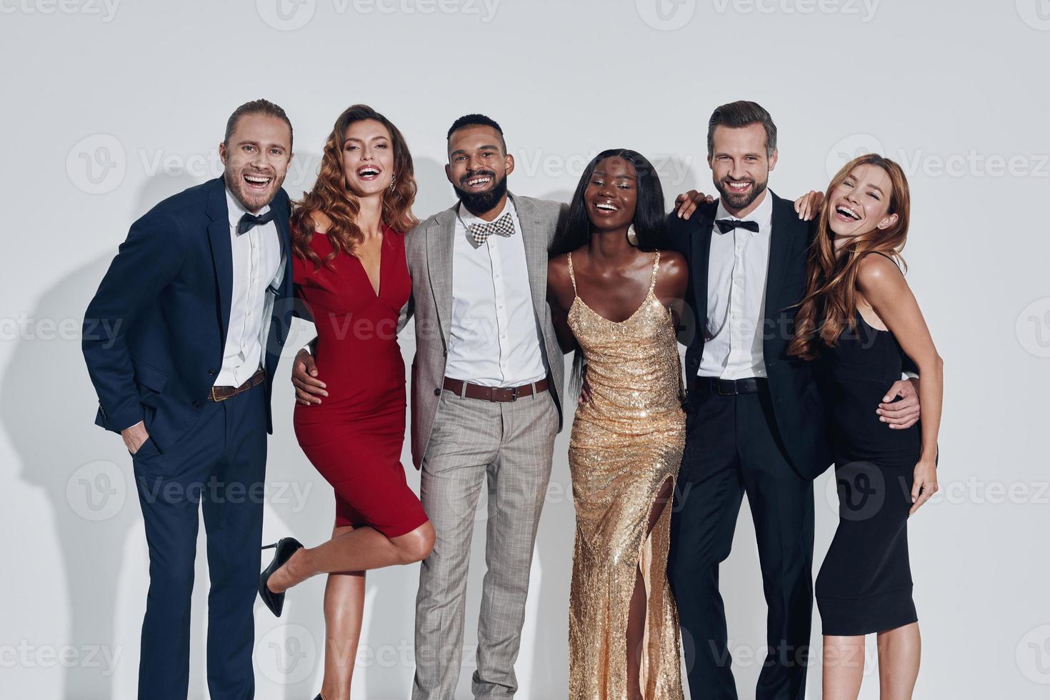 groupe de belles personnes en tenue de soirée se liant et souriant en se tenant debout sur fond gris photo