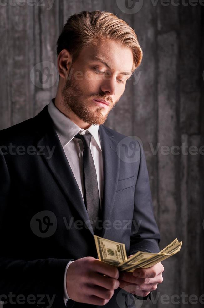 beau riche. beau jeune homme en tenue de soirée comptant de l'argent photo