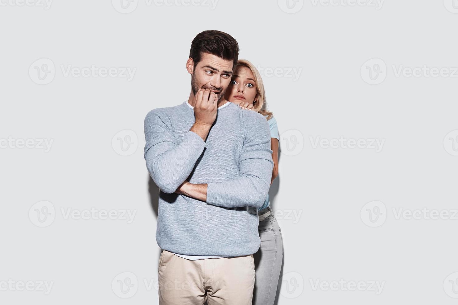 inquiet de quelque chose. jeune couple terrifié faisant une grimace en se tenant debout sur fond gris photo