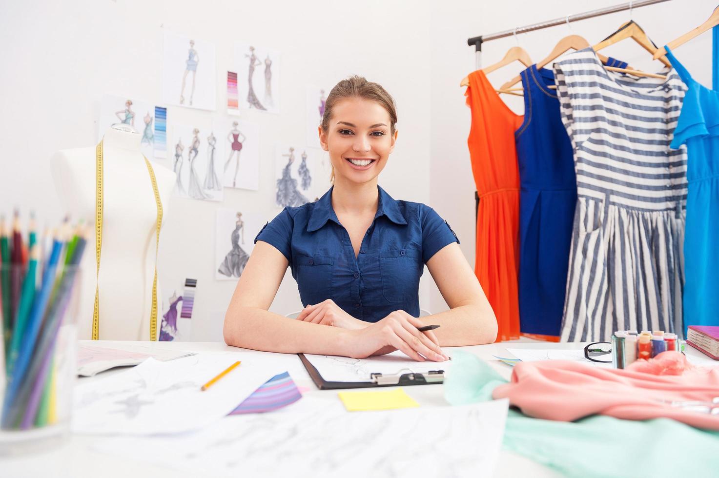 créateur de mode confiant. jolie créatrice de mode féminine regardant la caméra et souriante assise sur son lieu de travail photo