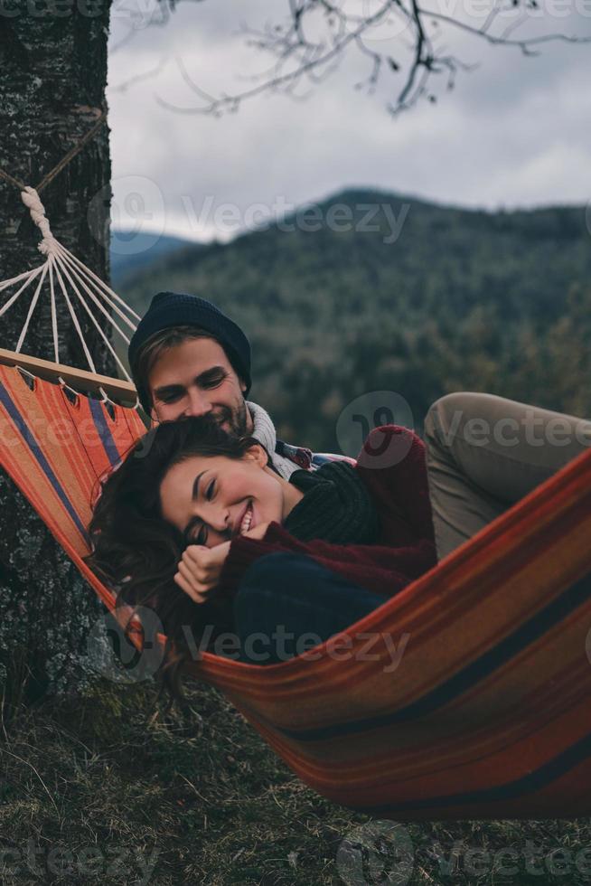 tout simplement amoureux. beau jeune couple embrassant et souriant en position couchée dans un hamac sous l'arbre photo