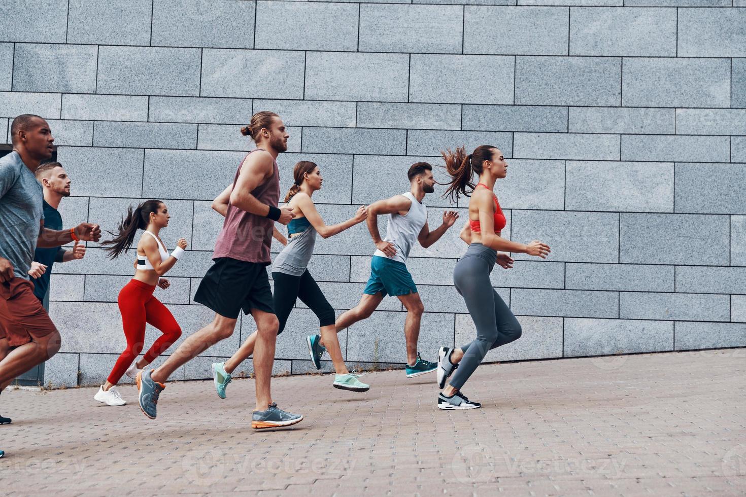 groupe de jeunes en vêtements de sport faisant du jogging tout en faisant de l'exercice sur le trottoir à l'extérieur photo