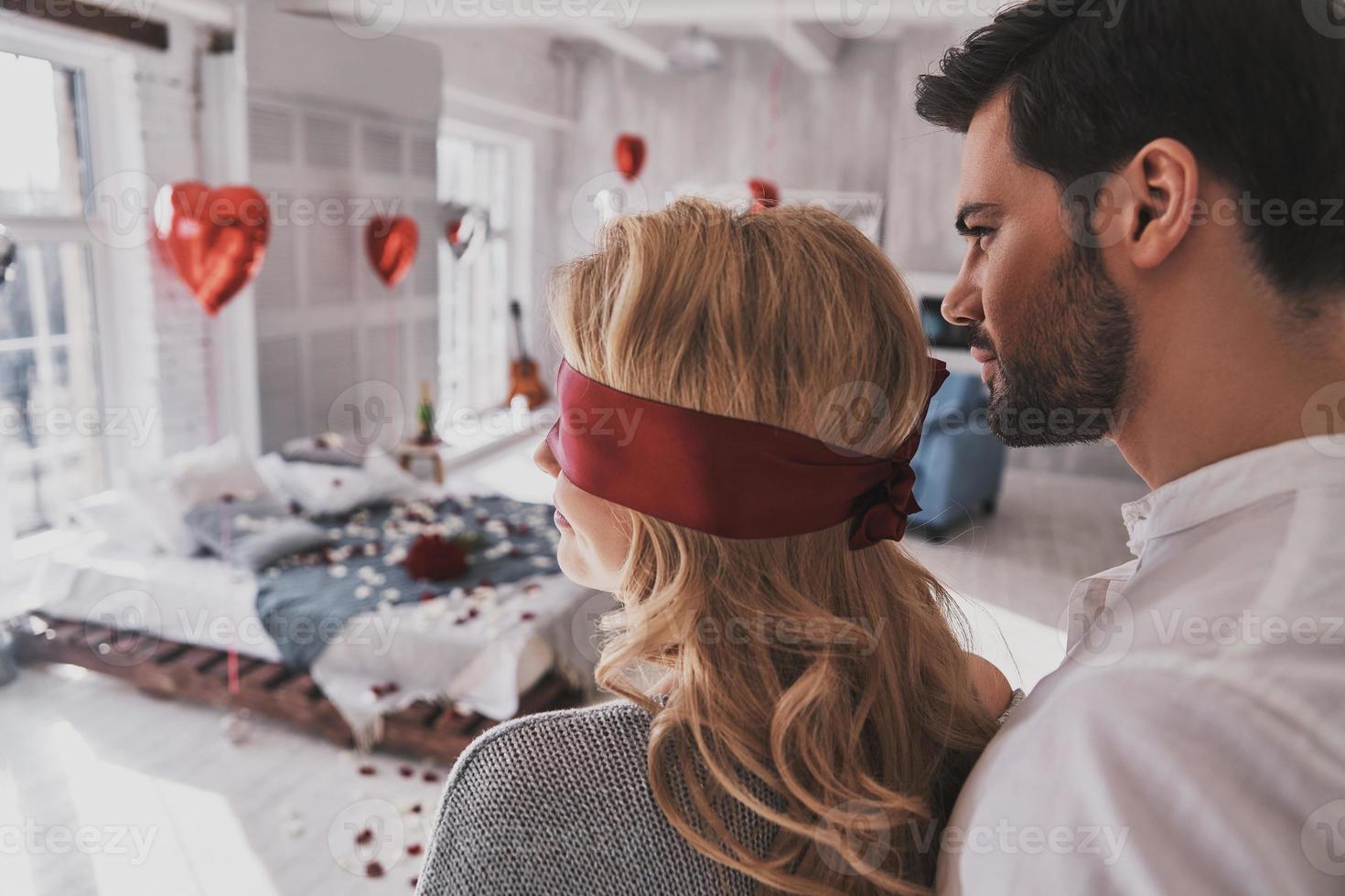 être patient. vue arrière d'une jeune femme debout avec les yeux bandés avec son petit ami tout en passant du temps à la maison photo