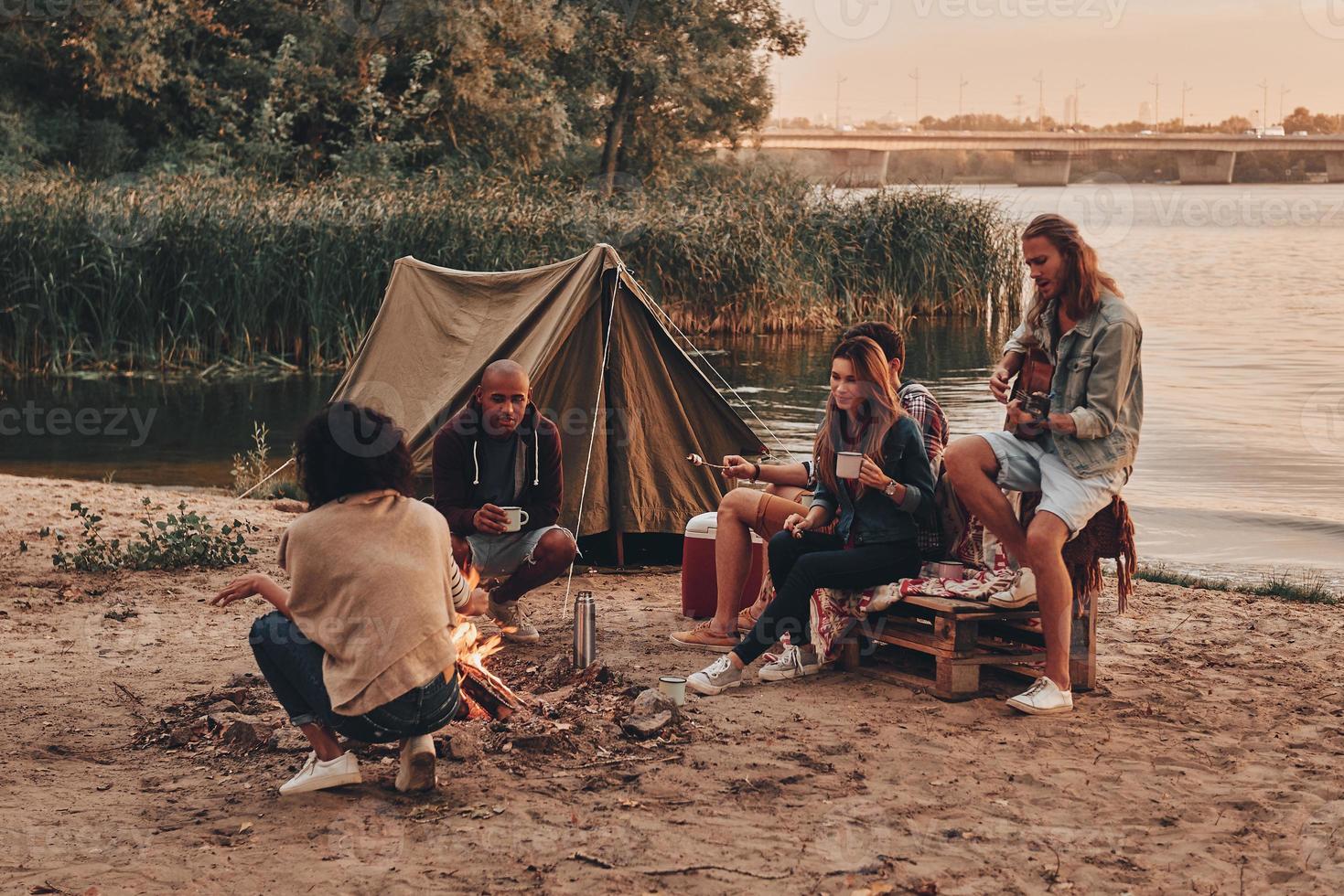 instants de joie. groupe de jeunes en tenue décontractée souriant tout en profitant d'une fête sur la plage près du feu de camp photo