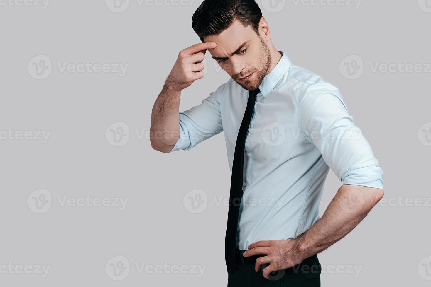 sentiment d'incertitude. jeune homme frustré touchant la tête avec la main et l'air incertain en se tenant debout sur fond gris photo