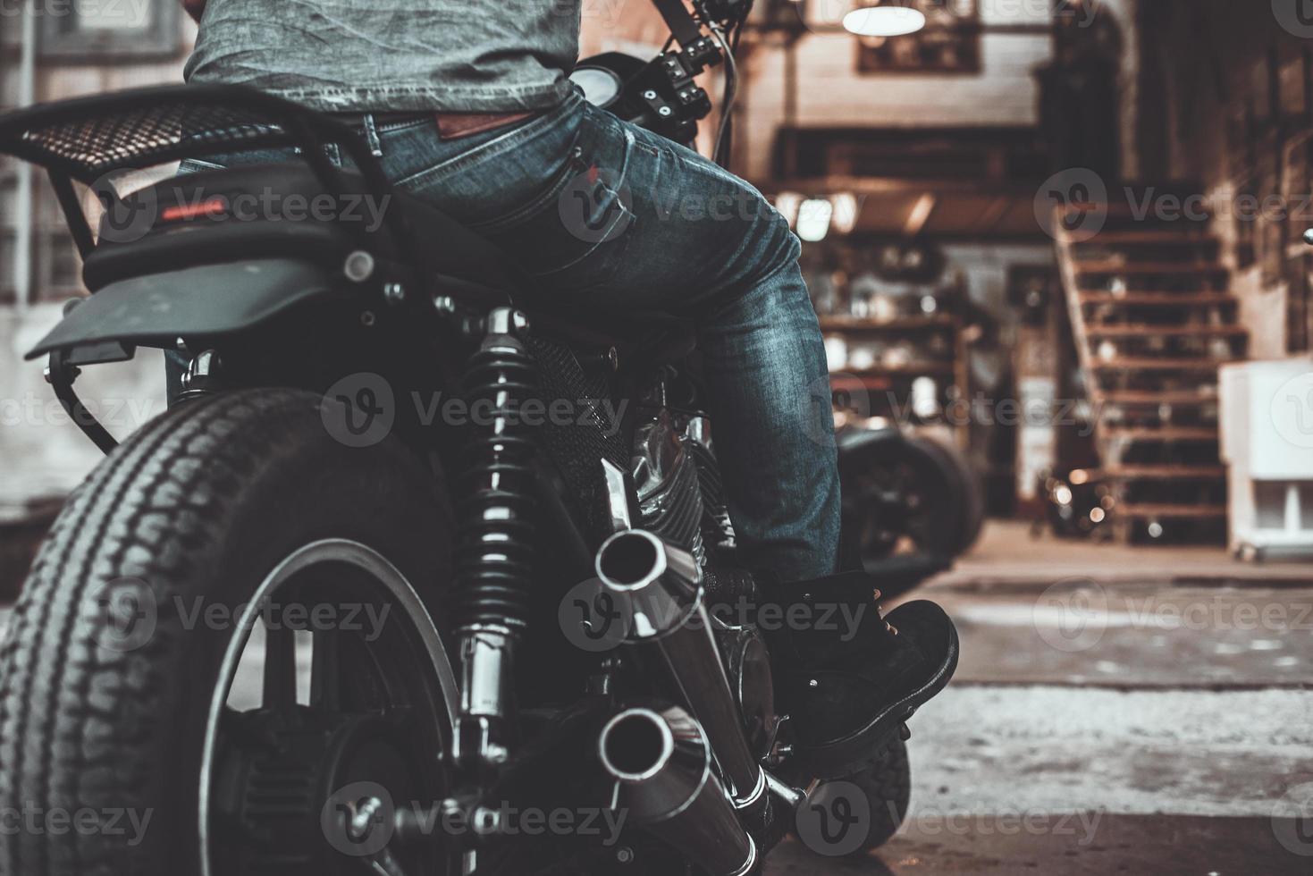sur le chemin de son garage. vue arrière en gros plan d'un homme assis sur son vélo avec un garage à motos en arrière-plan photo