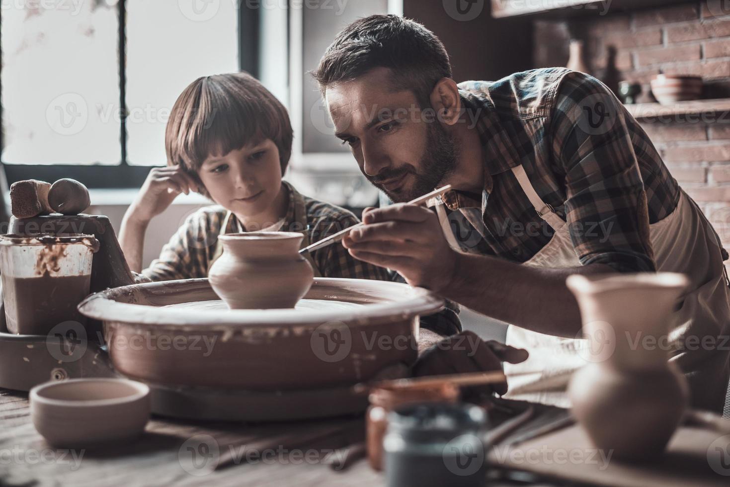 apprendre de nouvelles compétences. petit garçon regardant un jeune homme confiant s'appuyant sur un pot en céramique à la classe de poterie photo