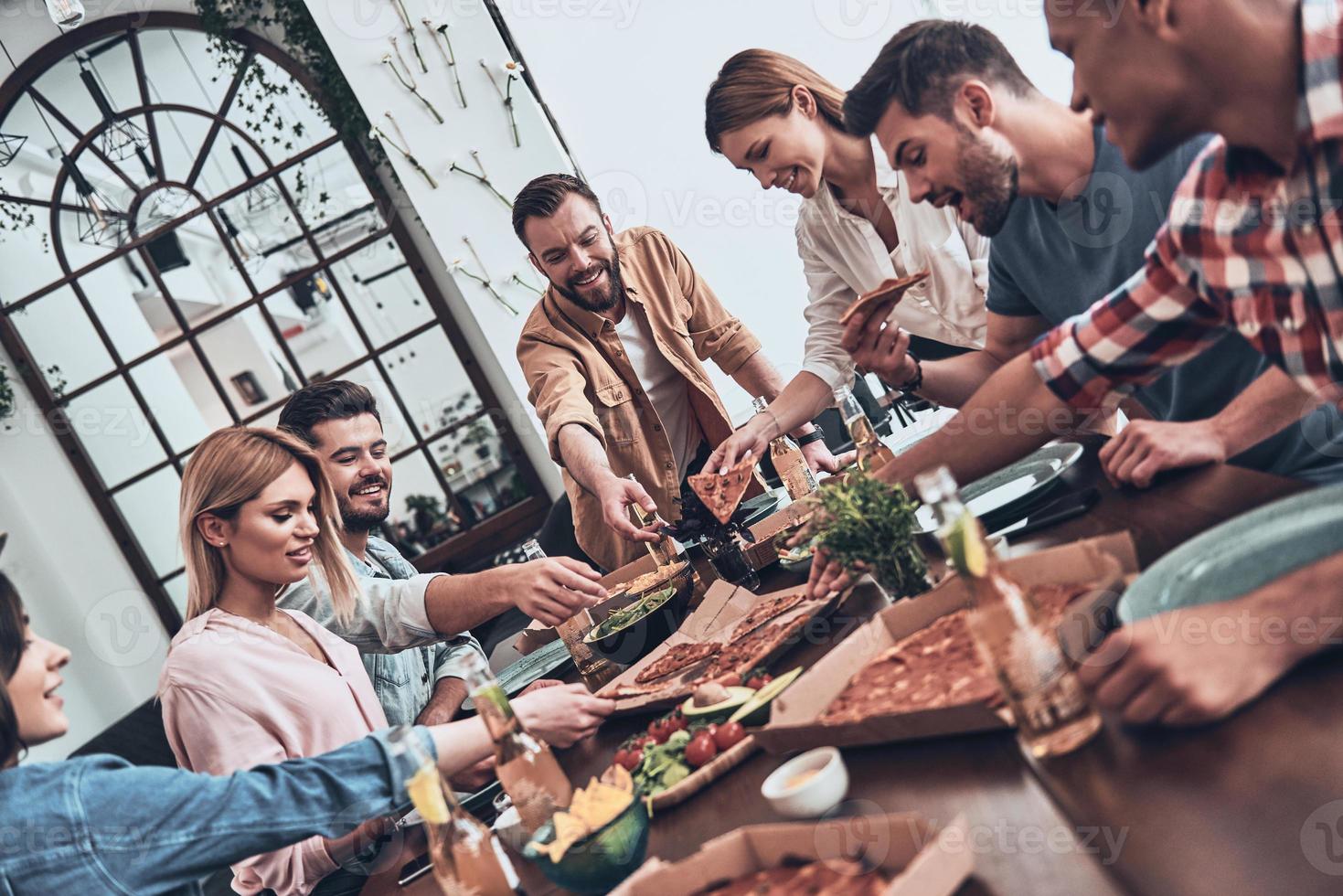 partager un bon repas. groupe de jeunes en tenue décontractée mangeant et souriant tout en ayant un dîner photo