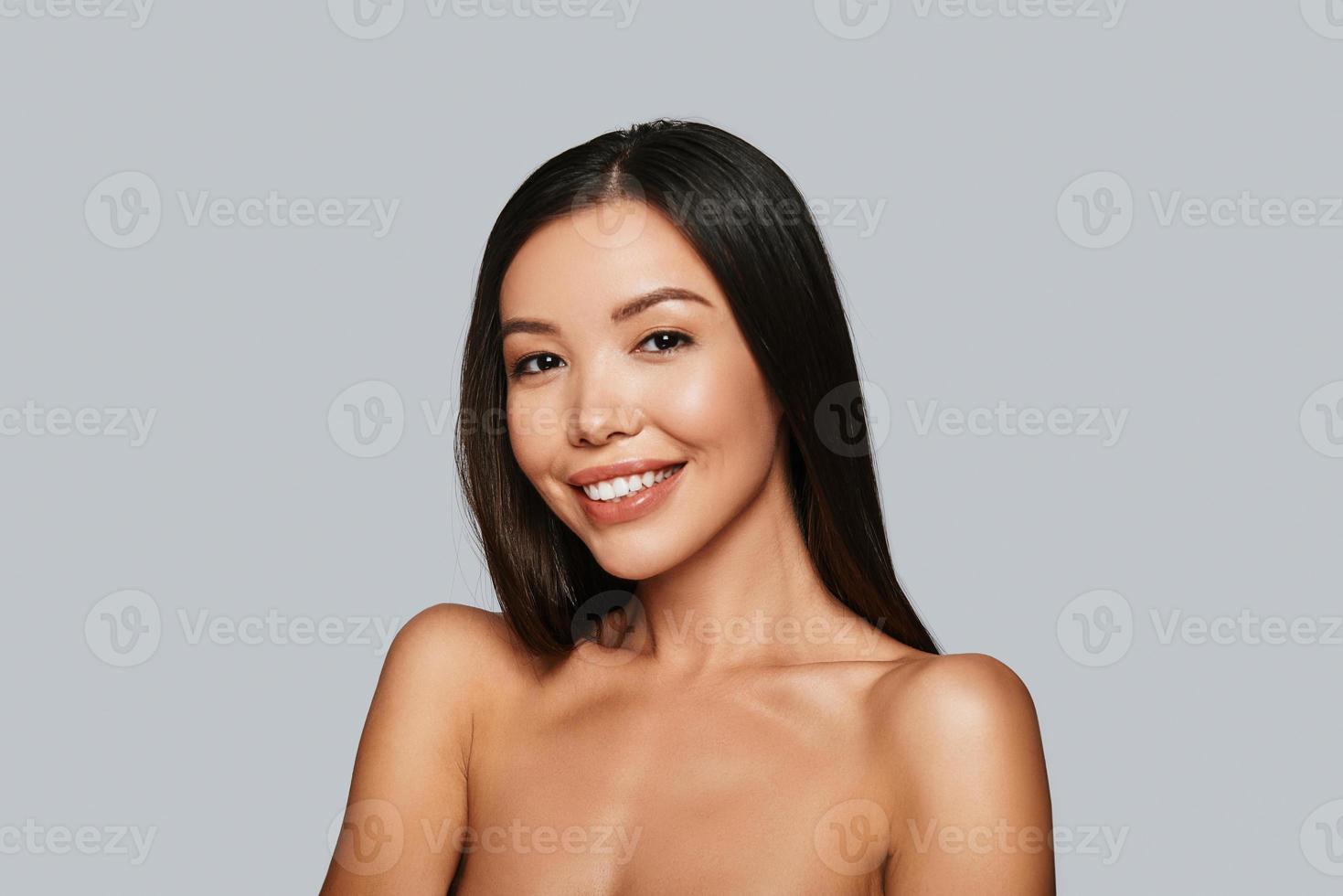 beauté brillante. belle jeune femme asiatique regardant la caméra et souriant en se tenant debout sur fond gris photo