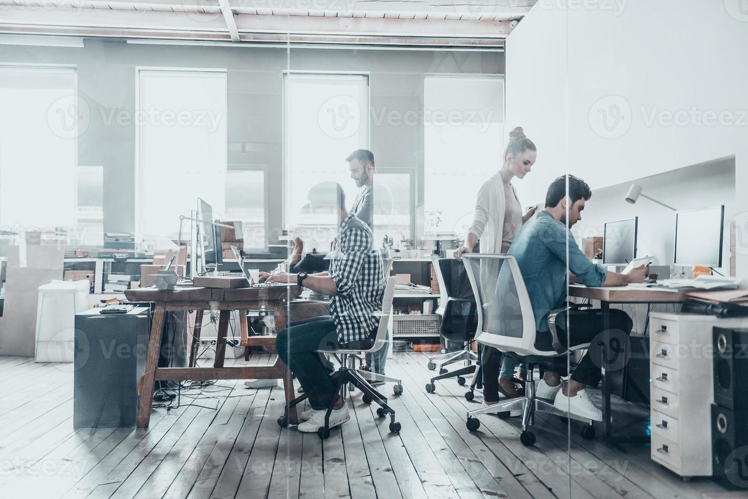 des professionnels performants. groupe d'hommes d'affaires utilisant des ordinateurs et communiquant tout en travaillant derrière le mur de verre dans le bureau de création photo