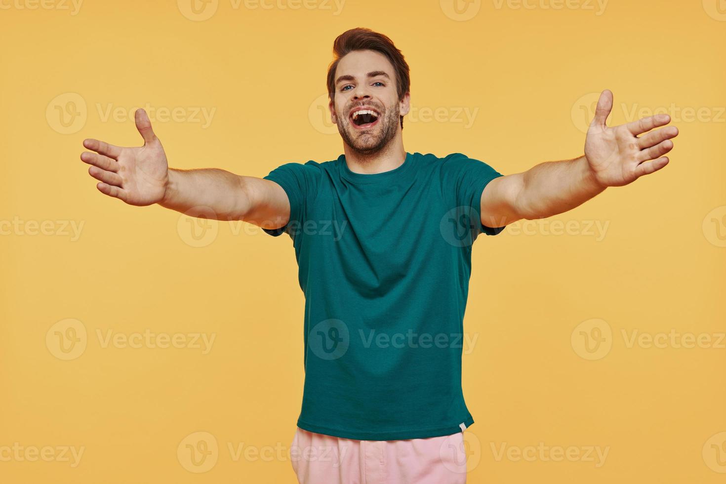 heureux jeune homme souriant dans des vêtements décontractés regardant la caméra et gesticulant câlin photo