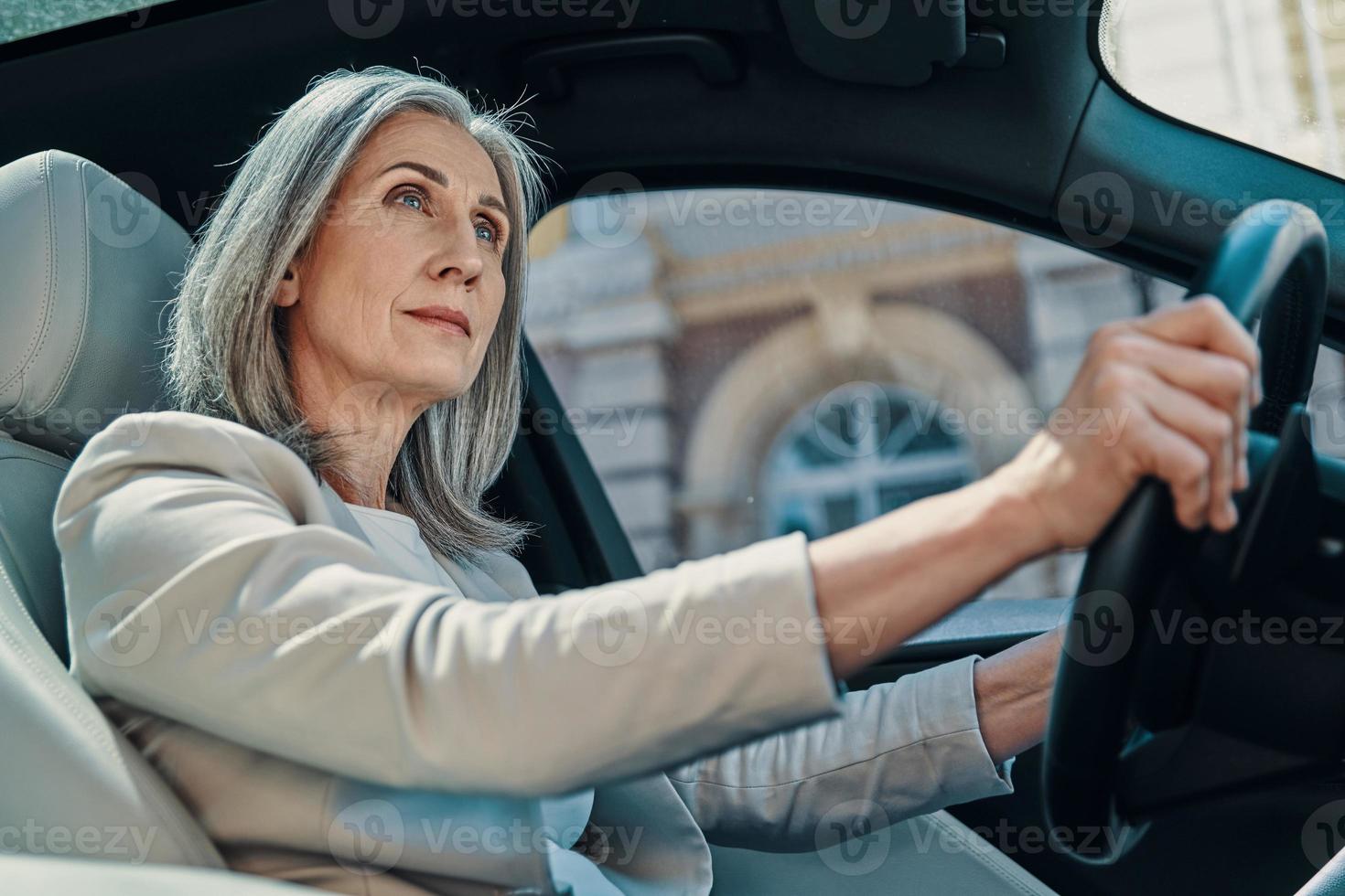 belle femme mûre en vêtements décontractés intelligents regardant loin en conduisant une voiture photo