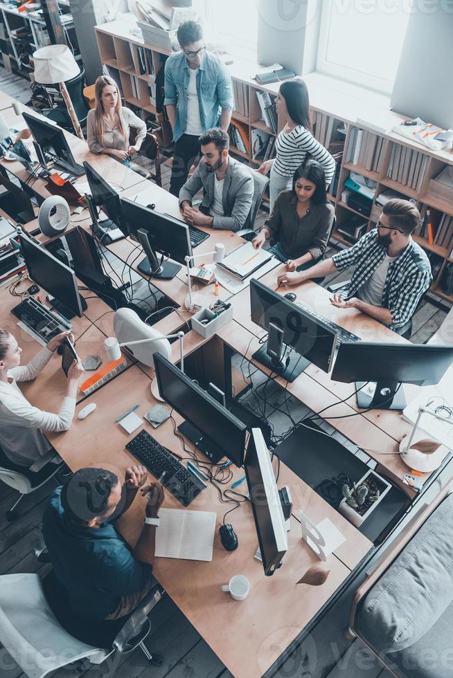 jeune équipe réussie au travail. vue de dessus d'un groupe de jeunes gens d'affaires en vêtements décontractés intelligents travaillant ensemble assis au grand bureau photo