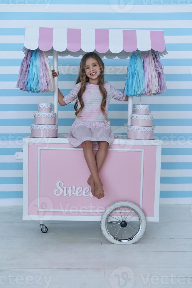 princesse sur chariot de bonbons. jolie petite fille regardant la caméra et souriante assise sur la décoration du chariot de bonbons photo