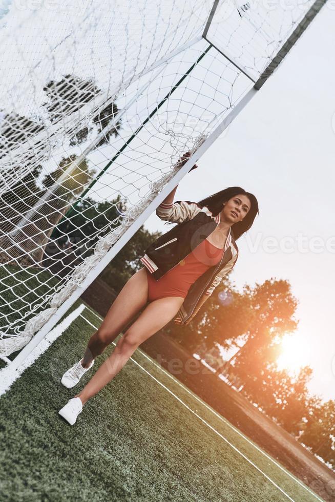 prêt à jouer. toute la longueur de la jolie jeune femme en bikini rouge posant près du poteau de but sur le terrain de football photo