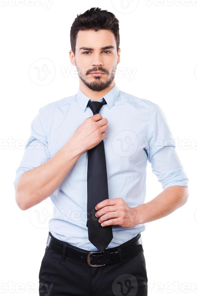 tout doit être parfait. confiant jeune homme en chemise et cravate regardant la caméra et ajustant sa cravate en se tenant debout sur fond blanc photo