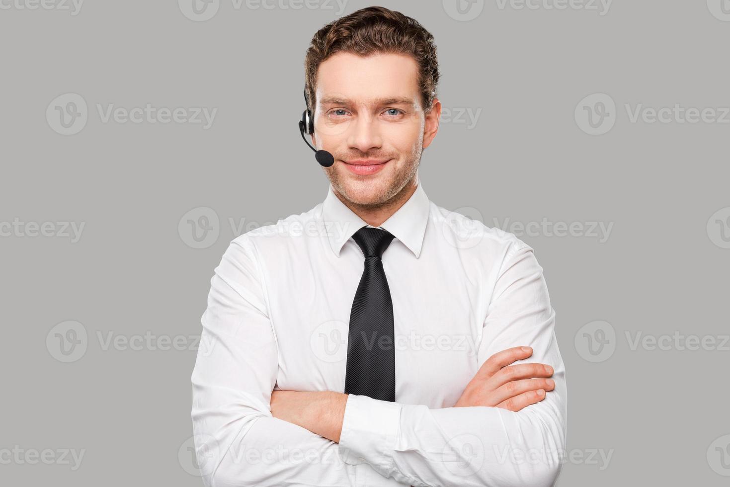 opérateur masculin. beau jeune homme en tenue de soirée et casque regardant la caméra et souriant en se tenant debout sur fond gris photo