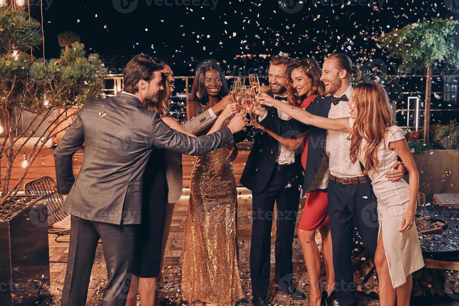groupe de gens heureux en tenues de soirée portant un toast au champagne avec des confettis volant tout autour photo