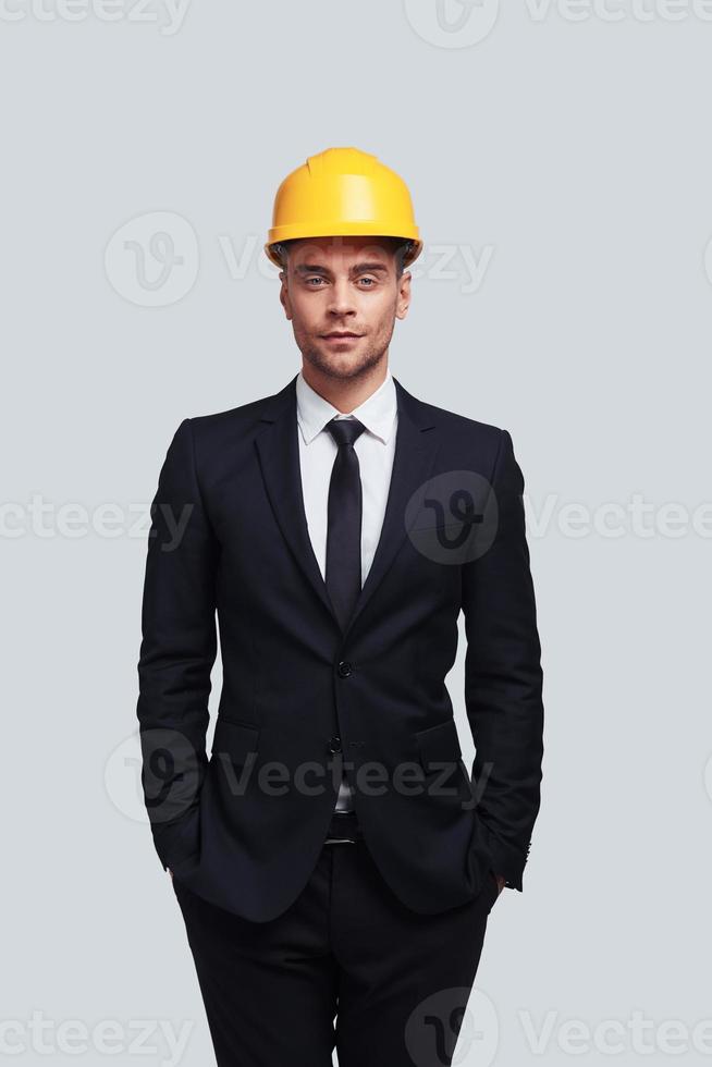 la sécurité passe avant tout. beau jeune homme en casque gardant les mains dans les poches et regardant la caméra en se tenant debout sur fond gris photo