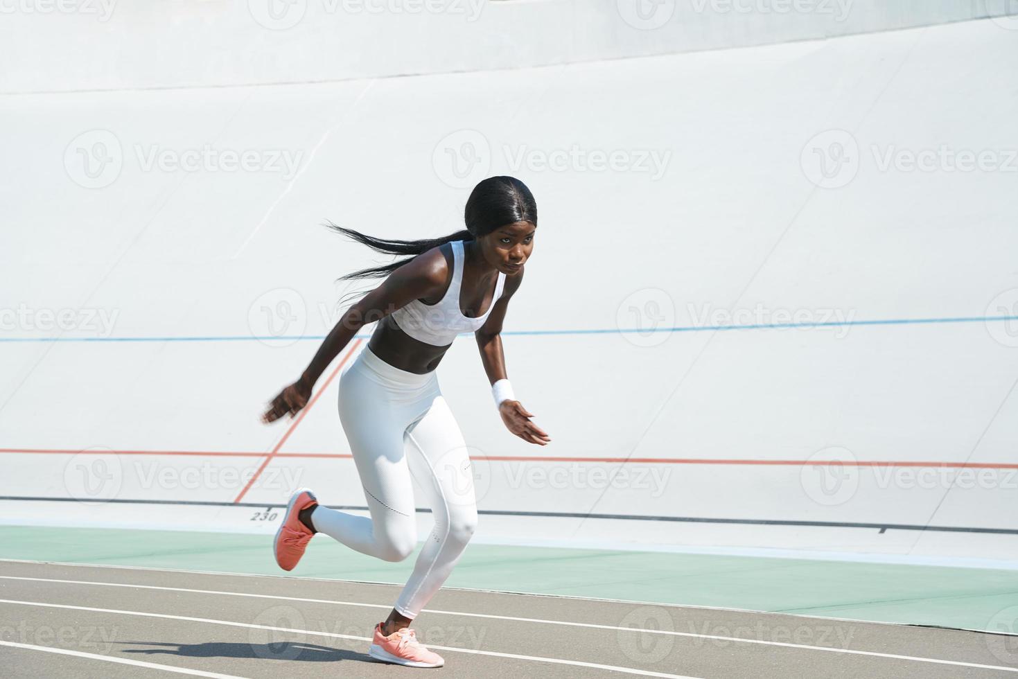 confiante jeune femme africaine en vêtements de sport courant sur la piste à l'extérieur photo