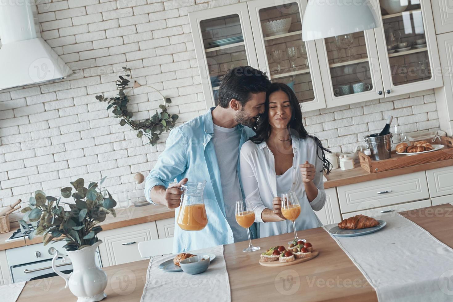heureux jeune couple préparant le petit déjeuner ensemble et souriant tout en passant du temps dans la cuisine domestique photo