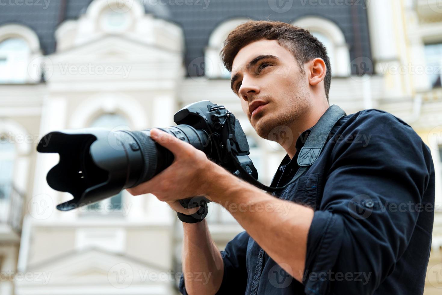 prêt à tirer. vue en contre-plongée d'un jeune homme tenant un appareil photo tout en se tenant à l'extérieur