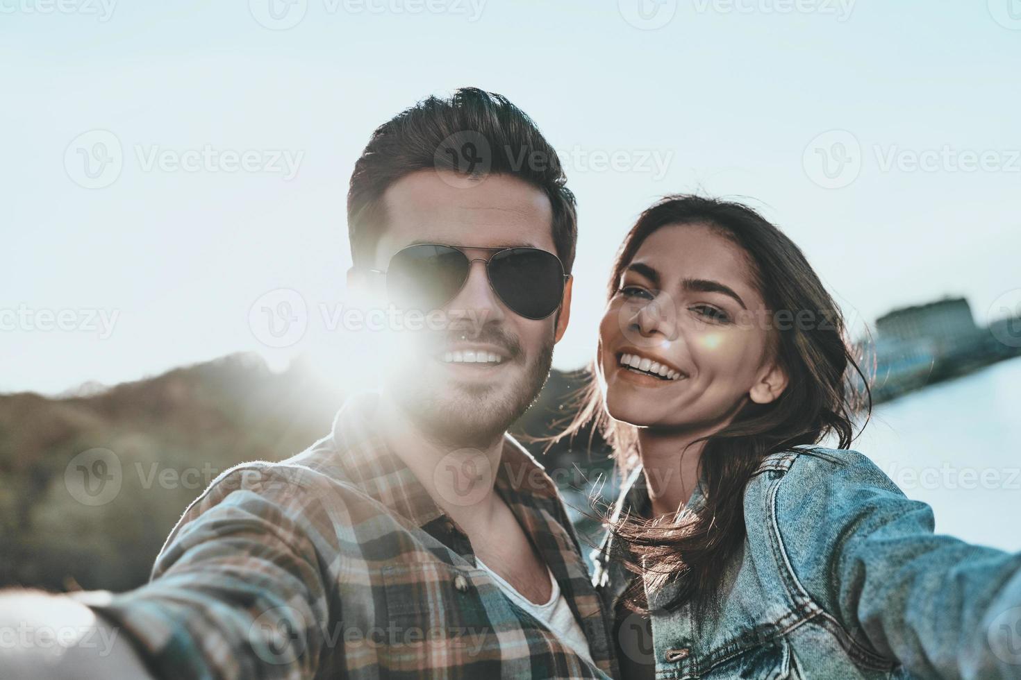 selfie avec ma chérie. autoportrait d'un beau jeune couple embrassant et regardant la caméra en se tenant debout sur le pont à l'extérieur photo