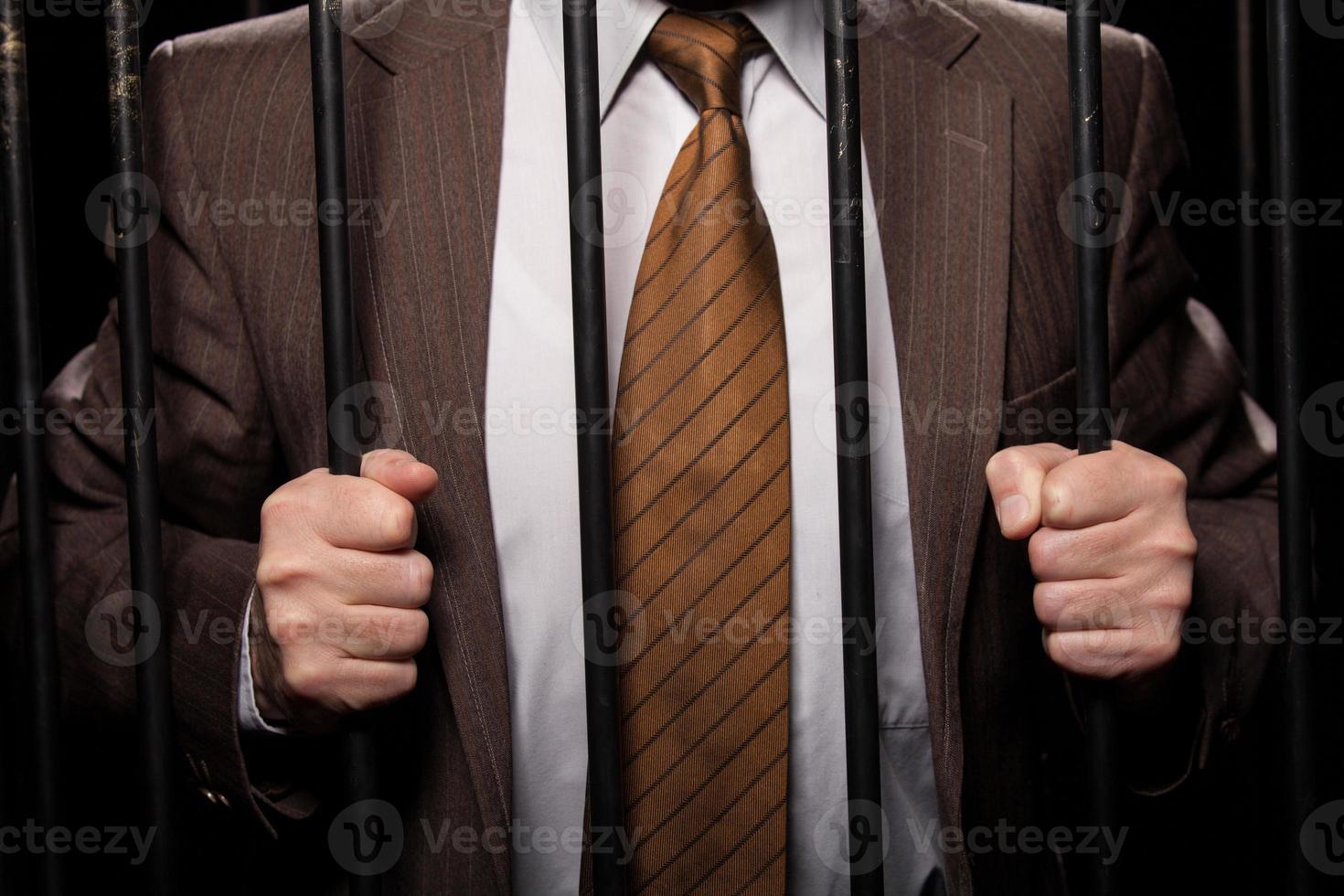 criminalité en col blanc. image recadrée d'un homme en tenue de soirée debout derrière une cellule de prison tout en étant isolé sur fond noir photo